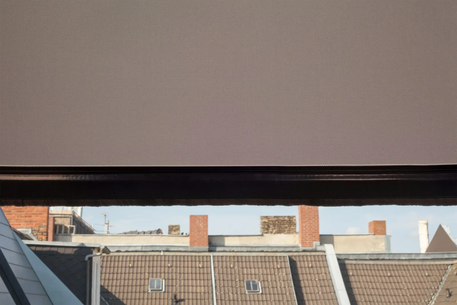 Blick aus dem Dachfenster über Berliner Dächer, darüber das halb geschlossene Rollo