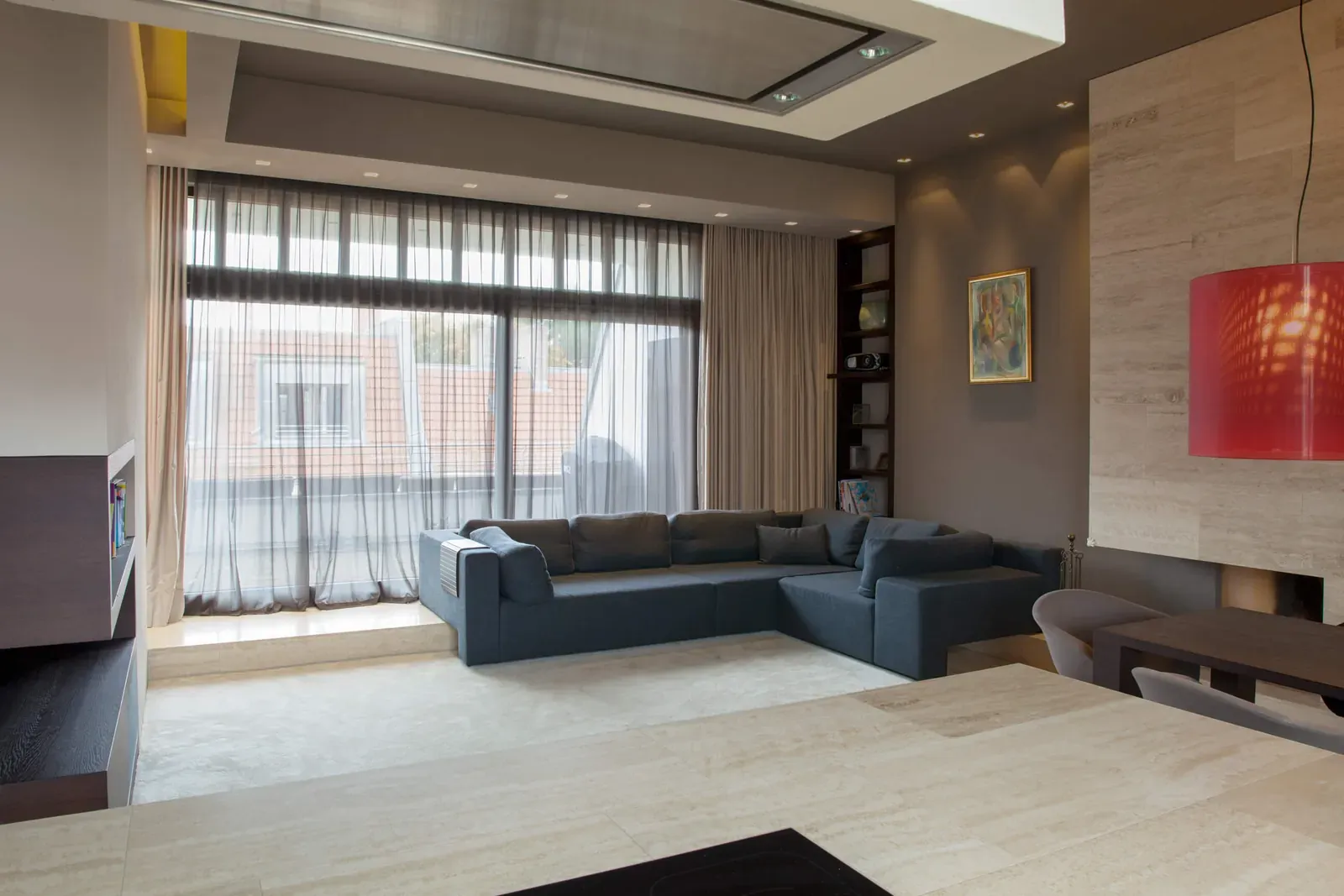 Wohnzimmer mit dunklem Sofa, bodenlangen Vorhängen und roter Pendelleuchte