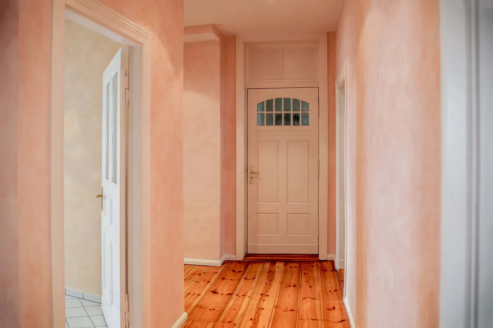Flur der Altbauwohnung mit rosé lasierten Wänden, weißen Türen und Dielenboden