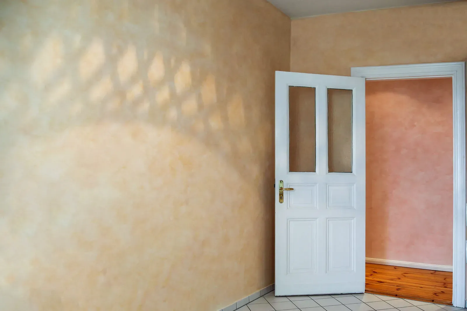Ocker lasierte Wand mit Lichtschatten neben einer geöffneten weißen Flügeltür