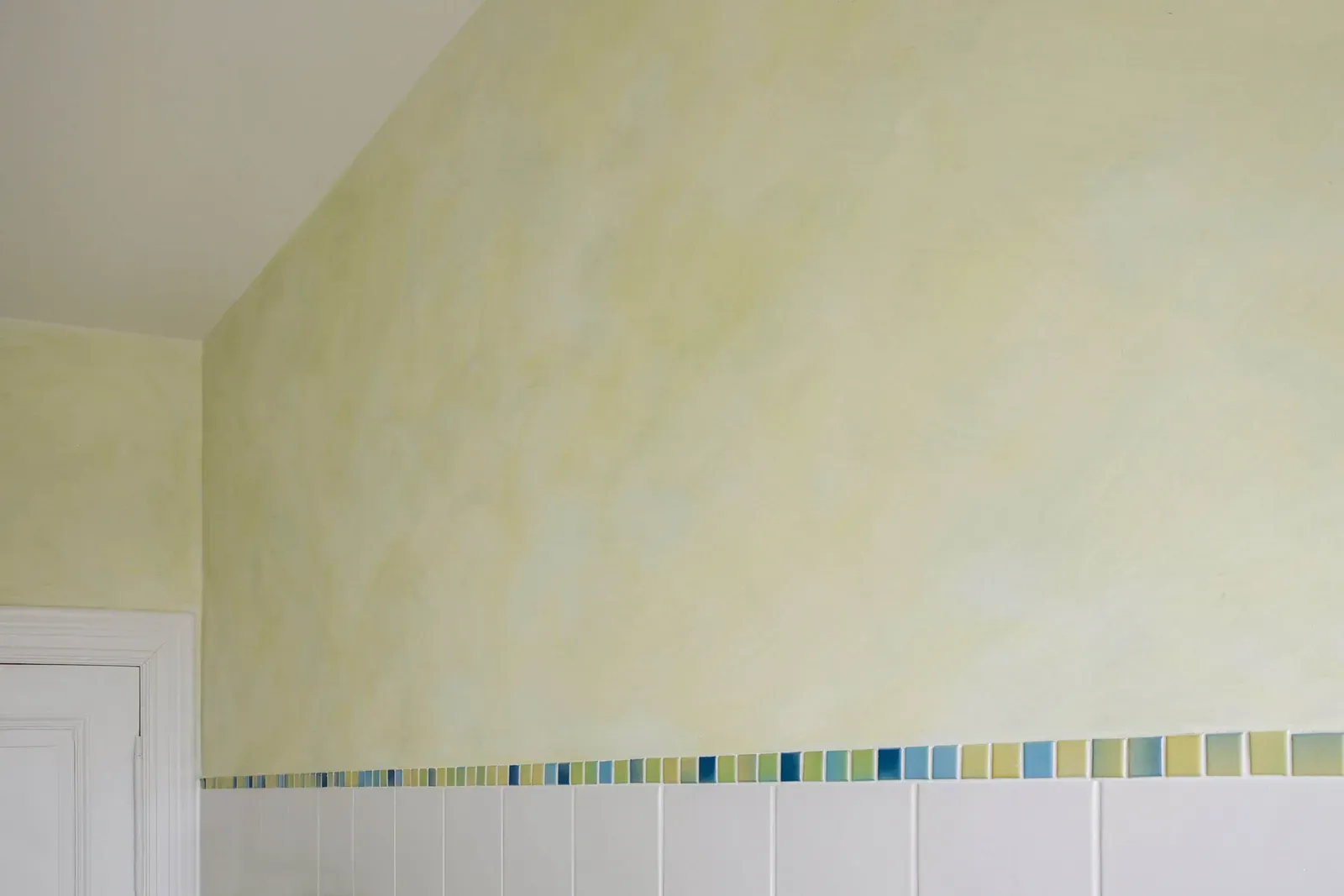 Gelb lasierte Wand über einer Fliesenbordüre in Blau- und Grüntönen
